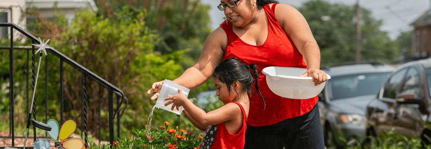 a little girl waters flowers with help from her mother