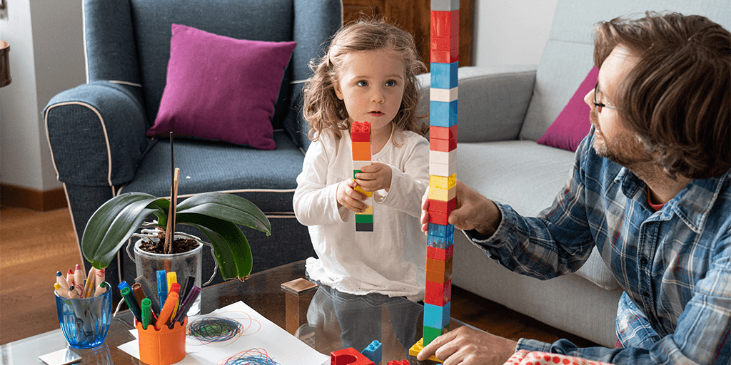 A young girl and man play with building blocks