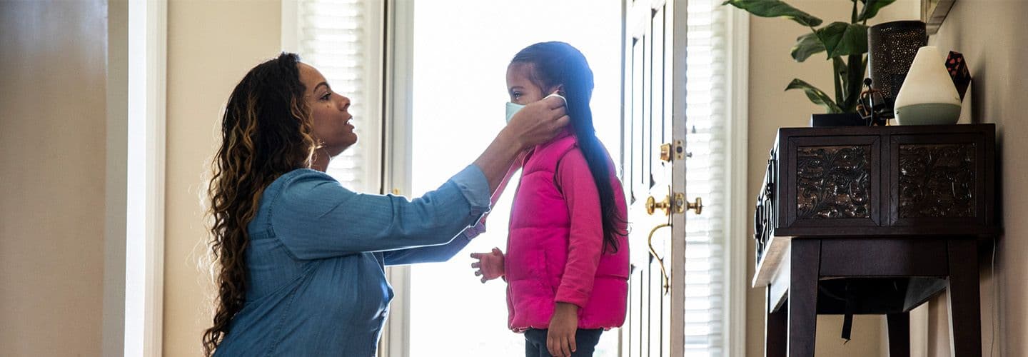 a mother helps her daughter put on a mask