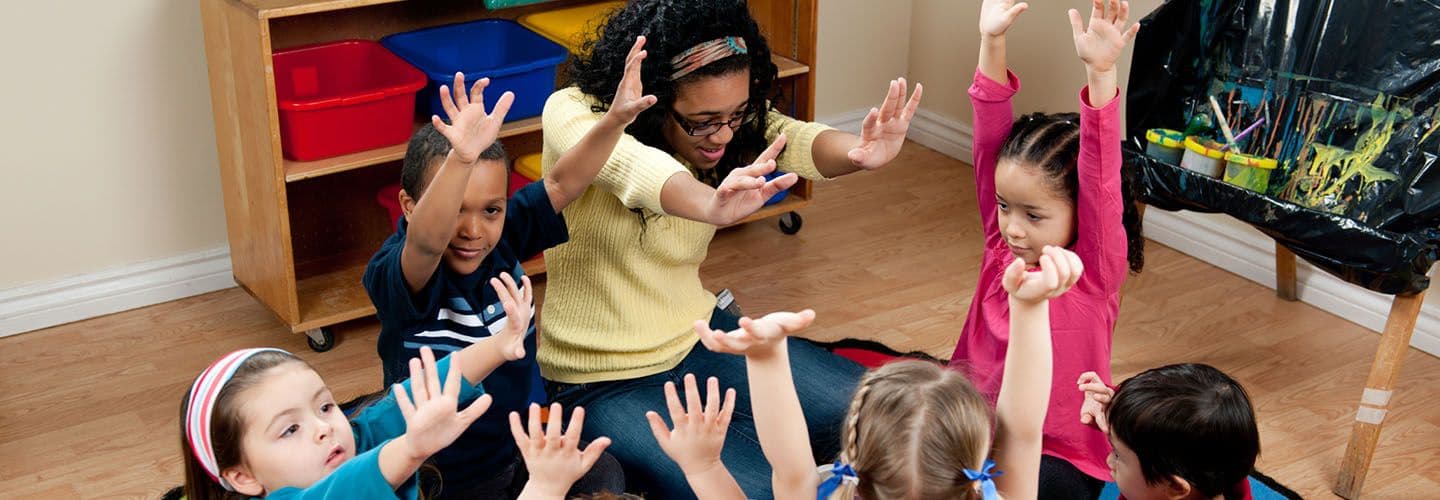 a teacher sits in a circle with a group of preschoolers