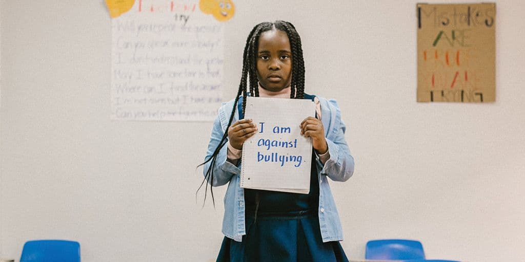 "a young girl stands holding a sign that reads ""I am against bullying"""