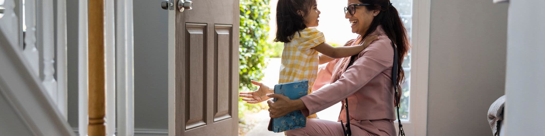 Toddler girl embracing mother in doorway as she gets home from work