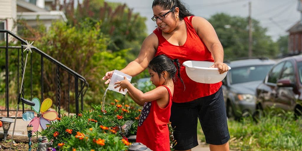 a little girl waters flowers with help from her mother