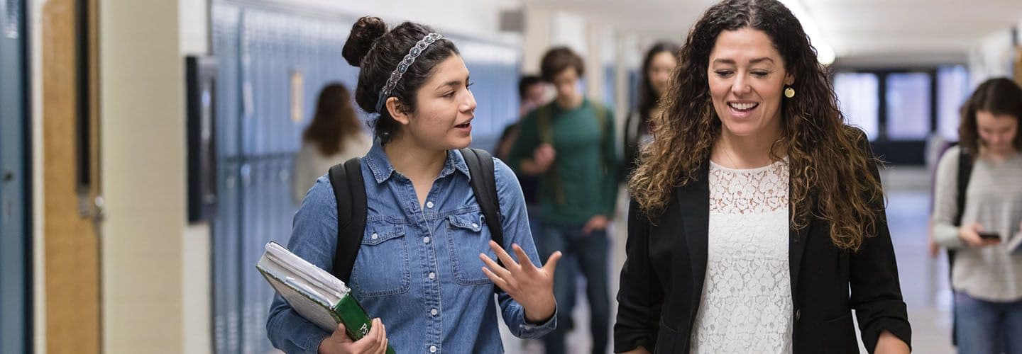 a teacher and young adult talk in the school hallway