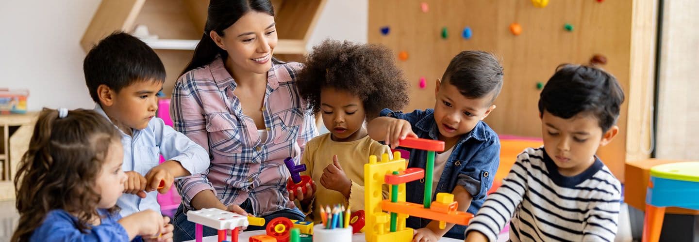a teacher sits with a group of young students who are playing with blocks