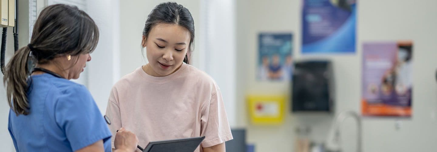 a young woman sits on an exam table while talking to her doctor