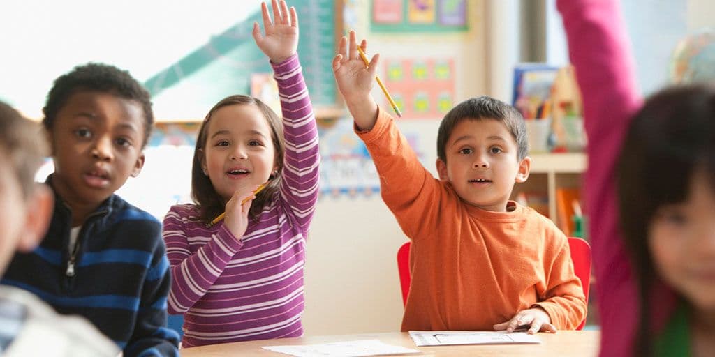 two young children raise their hands in class